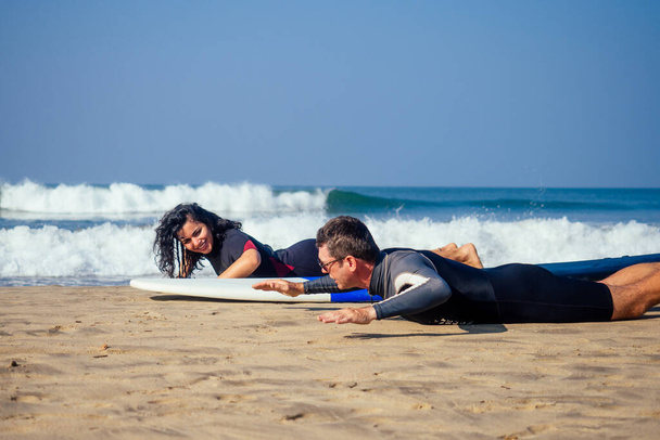 man instructor demonstrating how to stand up on surfboard to indian woman in surf class in Goa sea - Valokuva, kuva