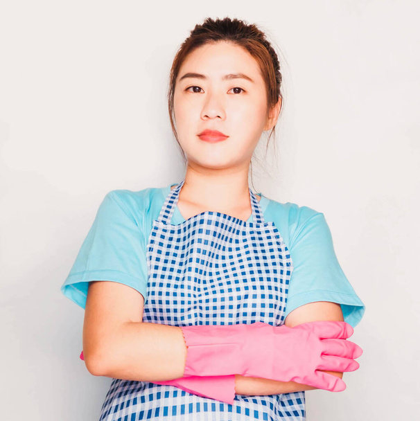 Junge schöne asiatische Hausmädchen trug blaues T-Shirt, Schürze und rosa Gummihandschuhe isoliert auf grauem Hintergrund - Foto, Bild