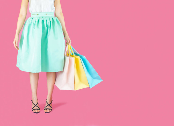 The  woman low body part wore blue skirt and black high heels. Carrying a shopping bag in many pastel colors on pink background selective focus - 写真・画像