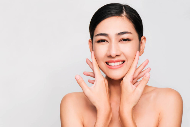 jong mooi aziatisch vrouw met schone en heldere huid, cosmetische schoonheid concept, handen aanraken op de wang, glimlachen en vriendelijk gezicht geïsoleerd op grijze achtergrond - Foto, afbeelding