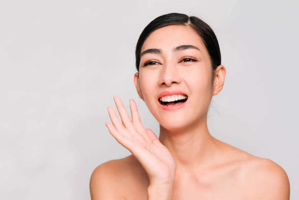 young beautiful asian woman with clean and bright skin, Cosmetic Beauty Concept,hands touch on the cheek, smiling and friendly face isolated on grey background - Fotó, kép