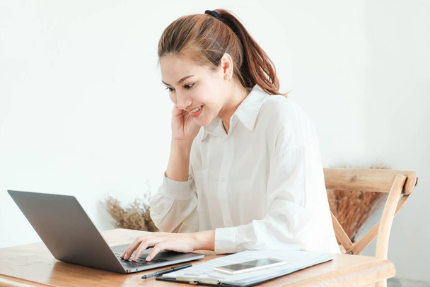 Beautiful asian business woman wearing white shirt, sitting on a desk with book. She was stressed and serious about something,Hand presses on the head,headache.Beautiful asian woman wore white shirt Sit and read a book,work on laptop at home in holid - Foto, afbeelding