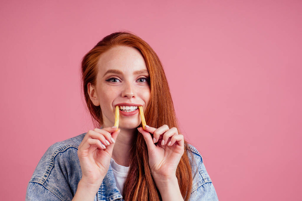 funny redhaired ginger woman with potatoes like canine tooth scaring, her hands want grab you in studio pink background. fright candies or life concept - Foto, Bild