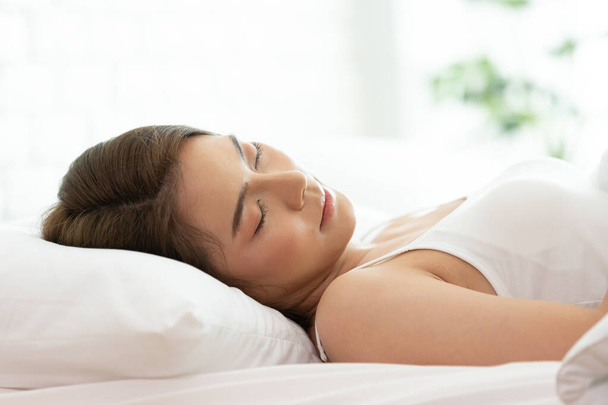 Piękna kobieta śpiąca na białym łóżku w sypialni, słodkie sny, ma zamknięte oczy, cieszy się dobrym odpoczynkiem w domu i spokojną atmosferą. Ludzie i koncepcja odpoczynku. - Zdjęcie, obraz