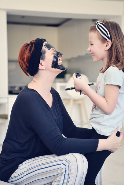 Family at home beauty treatment during coronavirus pandemic stay at home quarantine. Mother and little girl daughter  make a facial mask. - 写真・画像