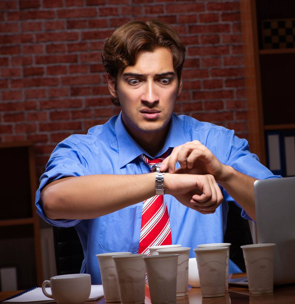 Empleado joven que bebe café trabajando en turno de noche
 - Foto, Imagen