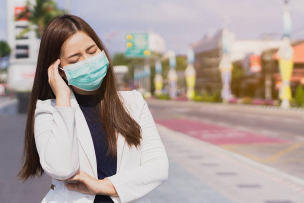 Die Geschäftsfrau hat Kopfschmerzen durch das Coronavirus und kann in der modernen Stadt nicht mehr arbeiten. Coronavirus und Luftverschmutzung pm 2.5 Konzept. - Foto, Bild