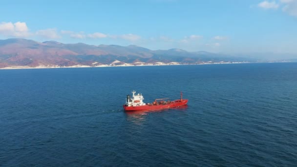 Vista aérea do navio de carga da cor vermelha que flutua no porto do mar, montanha no fundo
 - Filmagem, Vídeo