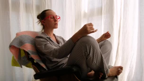 Kobieta w piżamie medytuje na krześle - Materiał filmowy, wideo