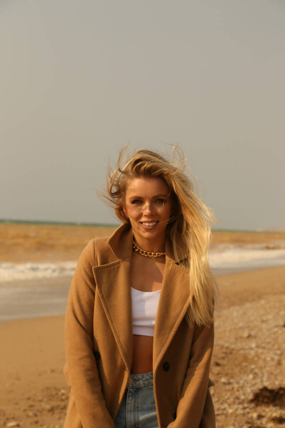 fashion outdoor photo of beautiful sexy woman with blond hair in elegant clothes walking along spring beach - Fotó, kép