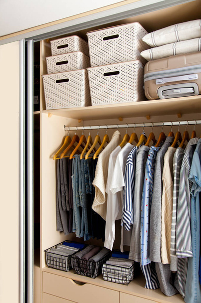 Wardrobe with perfect order clothes in blue and light shades on the hangers and things in containers. The concept of organizers and cleanliness in the house - 写真・画像