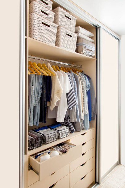Wardrobe with perfect order clothes in blue and light shades on the hangers and things in containers. The concept of organizers and cleanliness in the house - Foto, Bild
