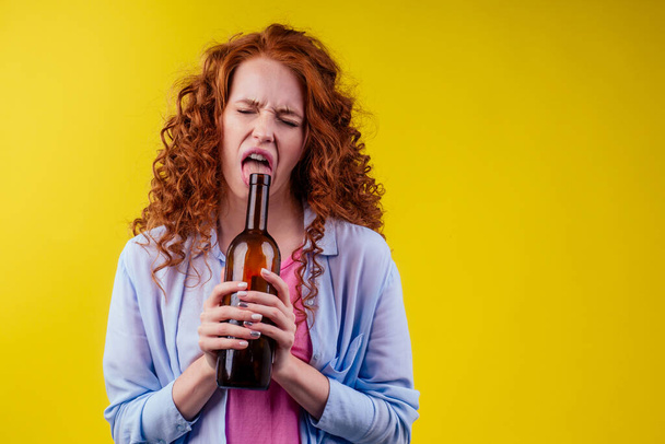 curly redhead ginger woman drinking beer and feeling bad mood in csudio yellow background - Фото, зображення