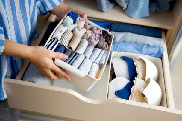 Unidentified neat housewife puts container with socks and pantyhose on wardrobe drawer during general cleaning by modern storage system. Concept of beautiful and comfortable organization - Photo, image
