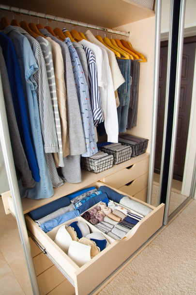 Wardrobe with perfect order clothes in blue and light shades on the hangers and things in containers. The concept of organizers and cleanliness in the house - Фото, зображення