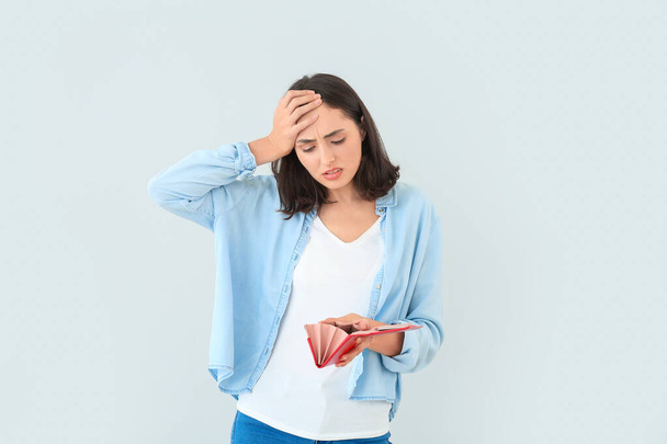 Worried young woman with empty wallet on light background - Photo, Image