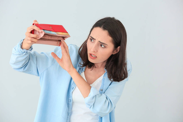 Worried young woman with empty wallet on light background - Фото, зображення