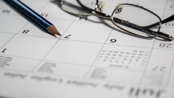 Closeup blue pencil and glasses on a calendar, business and finance concept. - 写真・画像