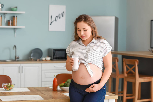 Beautiful pregnant woman with yogurt in kitchen - Fotoğraf, Görsel