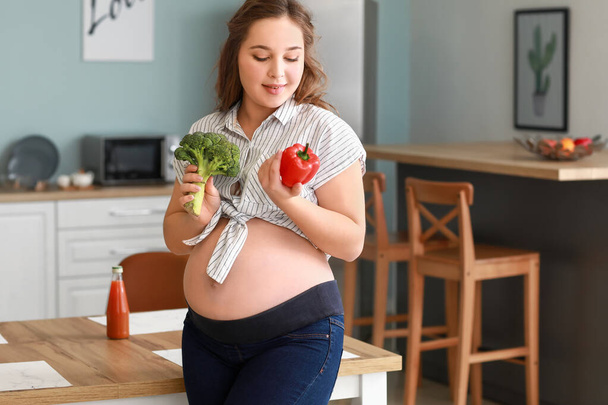 Beautiful pregnant woman with healthy food in kitchen - Photo, Image
