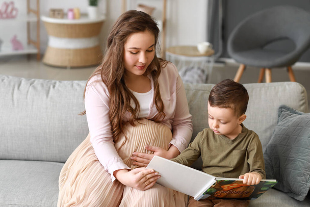 Hermosa mujer embarazada con su pequeño hijo leyendo libro en casa
 - Foto, imagen