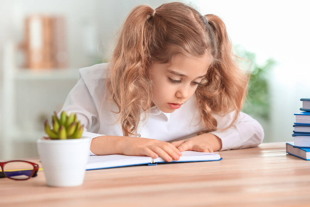 Roztomilá malá školačka dělá úkol na stole ve třídě - Fotografie, Obrázek