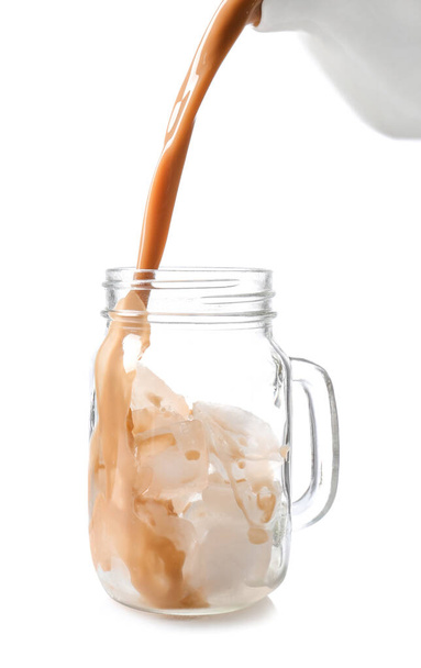 Gieten van koffie in metselaar pot met ijsblokjes op witte achtergrond - Foto, afbeelding