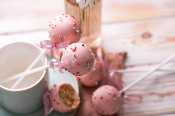 Cake pops in a light key in a beautiful utensil with pink chocolate cream and flowers on a wooden background. Tasty food - Photo, Image