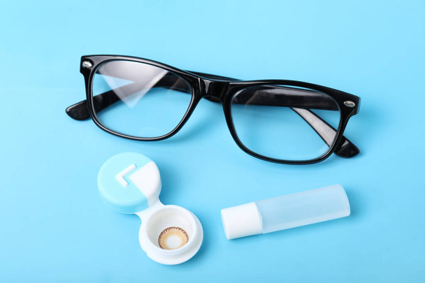 Container with contact lenses, solution and eyeglasses on color background - Photo, Image
