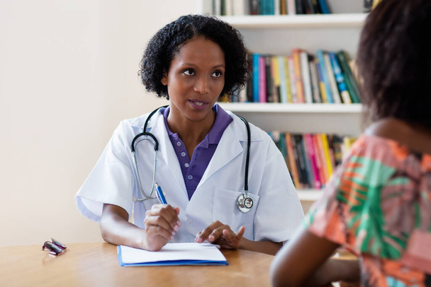 Rijpe Afro-Amerikaanse vrouwelijke arts uitleggen coronavirus symptomen aan de patiënt in het ziekenhuis - Foto, afbeelding