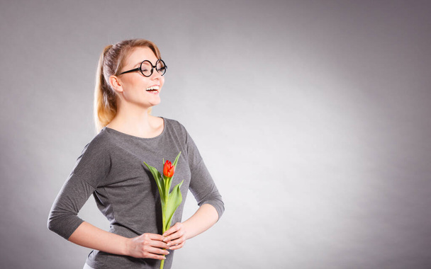 Felicidad y satisfacción con la vida. Mujer rubia usando gafas con tulipán verde rojo. Feliz alegría chica sintiendo primavera tiempo sosteniendo hermosa flor. - Foto, Imagen