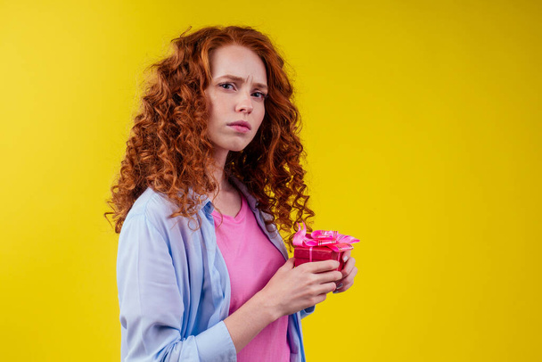 frowning redhaired ginger curly woman holding gifts boxes and dont want give it the in studio yellow background - Photo, image