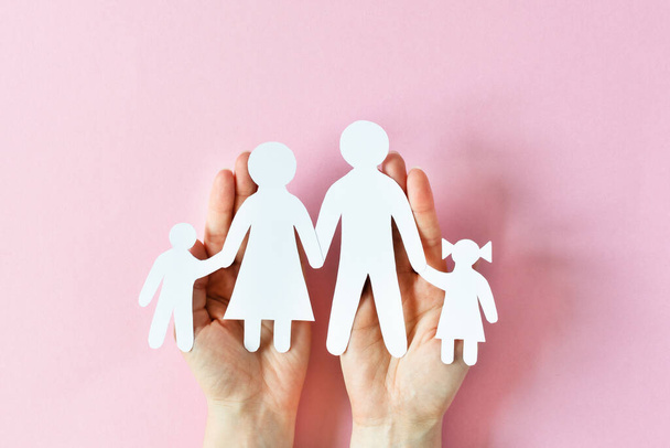 Nő tartja a papír család a kezében felső nézet rózsaszín háttér. Szerelem és kapcsolatok fogalma. - Fotó, kép