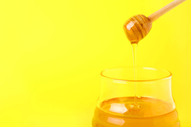 Honey dripping from dipper into jar on color background - Photo, Image