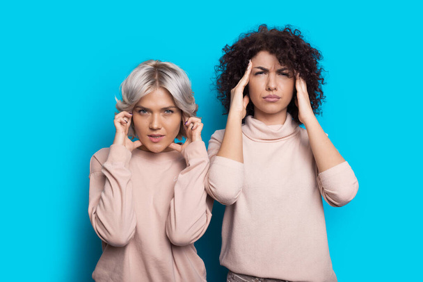 Mulheres caucasianas pensativas com cabelo encaracolado tocando a cabeça pensando em algo e posando em uma parede azul
 - Foto, Imagem