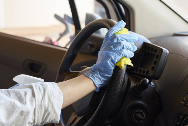 Kobieta w gumowej rękawicy dezynfekującej kierownicę samochodu. Czyszczenie pojazdu wewnątrz dla ochrony przed chorobą Coronavirus. Epidemia - Zdjęcie, obraz