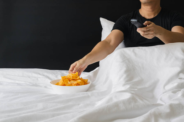 Chipsy ziemniaczane mieszające się z wodorostami w białej misce położyć na łóżku na przekąskę podczas oglądania filmu na łóżku. Zostań w domu.. - Zdjęcie, obraz