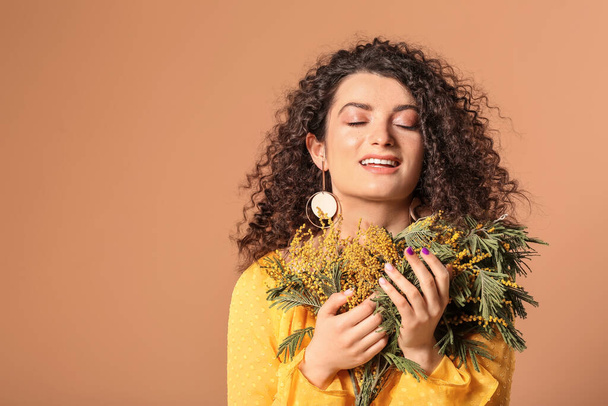 Mladá žena s krásnými kudrnaté vlasy a květiny na barevném pozadí - Fotografie, Obrázek