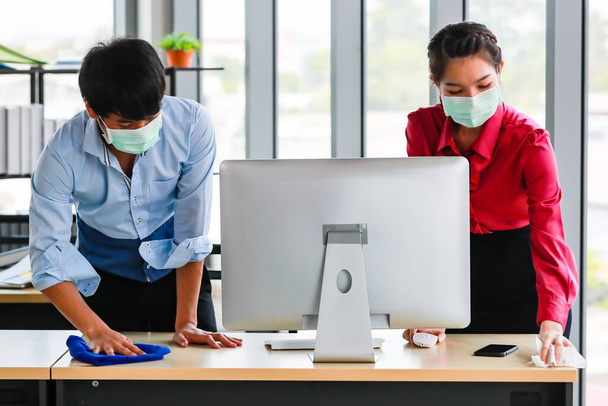 Współpracownicy noszący maski higieniczne czyszczą i sterylizują narzędzia biurowe i sprzęt w celu wyeliminowania ryzyka chorób i wirusów w miejscu pracy. Pomysł na dezynfekcję miejsca dla bezpieczeństwa. - Zdjęcie, obraz