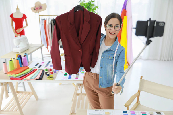 Genç ve güzel Asyalı moda tasarımcısı müşterisiyle yeni takım elbise koleksiyonunu canlı olarak gösteriyor. Koleksiyonunu dünyanın dört bir yanındaki insanlara satabilir.. - Fotoğraf, Görsel