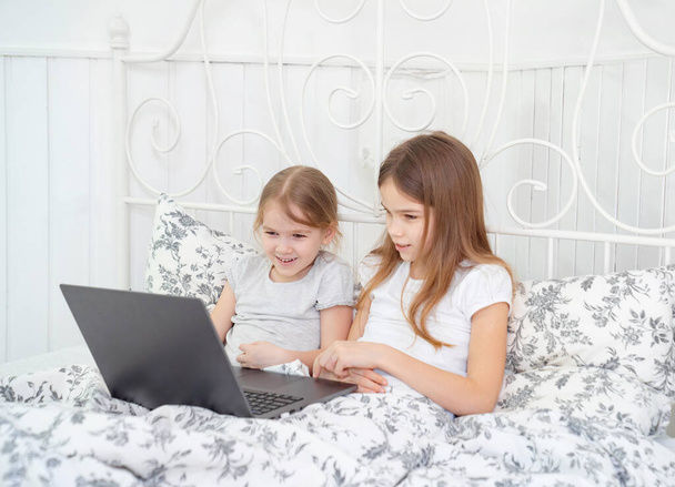 sisters play on computer online at home bed. - Фото, изображение