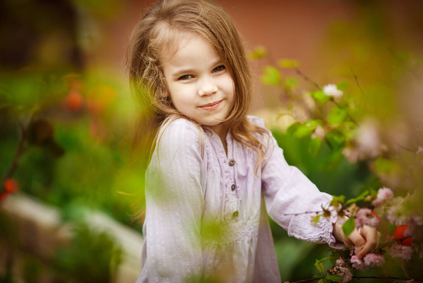 beautiful kid girl in garden with pink almond bush - 写真・画像