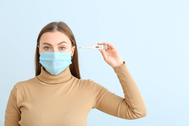 Woman in protective mask and with thermometer on color background. Concept of epidemic - Photo, Image