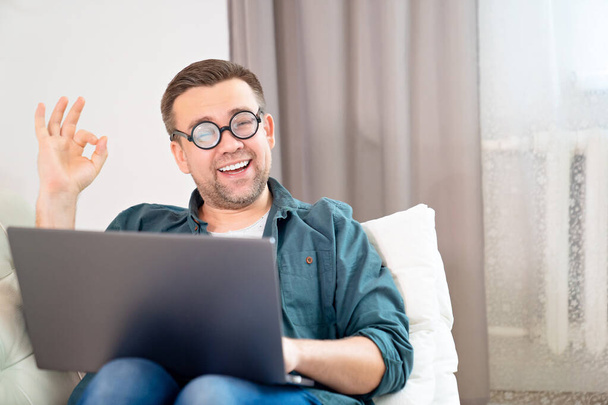 man freak with glasses working online on couch.  - Foto, afbeelding