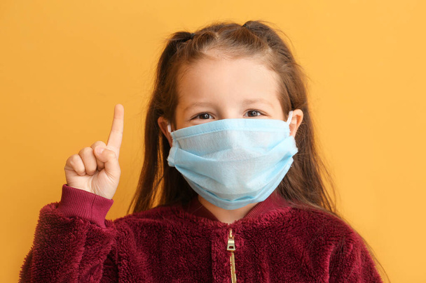 Little girl in protective medical mask and with raised index finger on color background - Fotó, kép