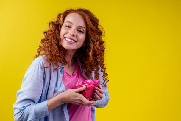 amazed redhaired ginger curly woman holding gifts boxes and feeling shock emotions in studio yellow background - Fotó, kép