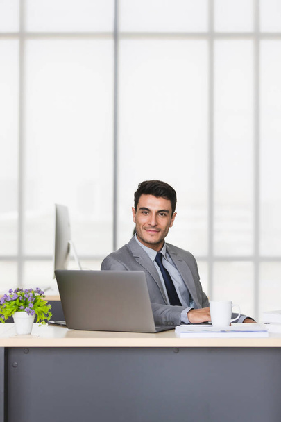 現代のオフィスで机の上にコーヒーカップと座って黒のスーツでハンサムな白人ビジネスマンの垂直イメージ. - 写真・画像