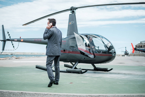 Бизнесмен разговаривает по телефону возле частного вертолета
 - Фото, изображение