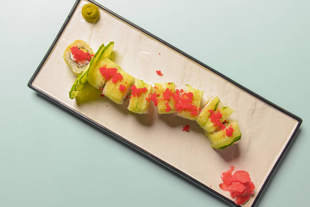 Green dragon sushi roll with eel, avocado, cucumber, wasabi sauce and ginger served on a white rectangular plate. - Fotó, kép