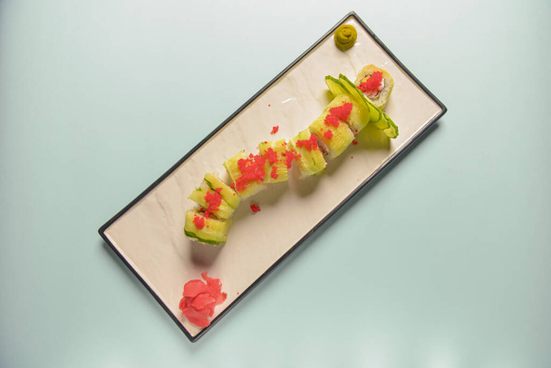 Green dragon sushi roll with eel, avocado, cucumber, wasabi sauce and ginger served on a white rectangular plate. - Photo, image